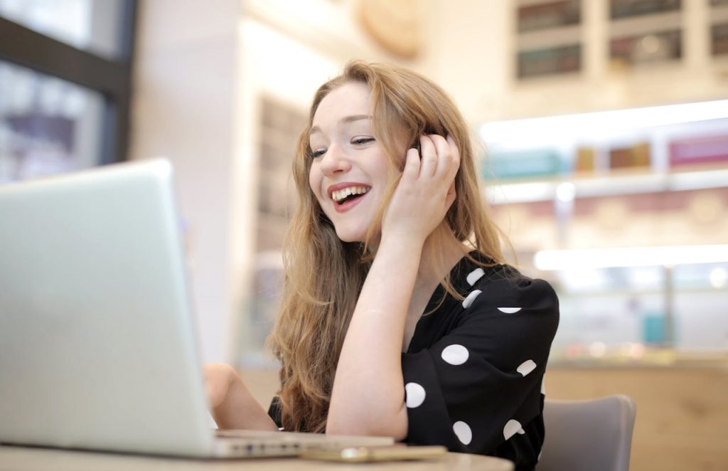 woman-in-black-and-white-polka-dots-dress-sitting-by-the-table-using-macbook-3783839 mujer muy contenta alojando su pagina web